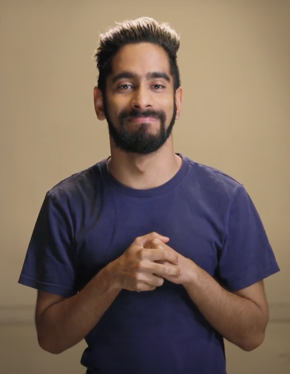 amar is a bipoc person. he smiles in a blue tshirt, holding his hands together on his chest