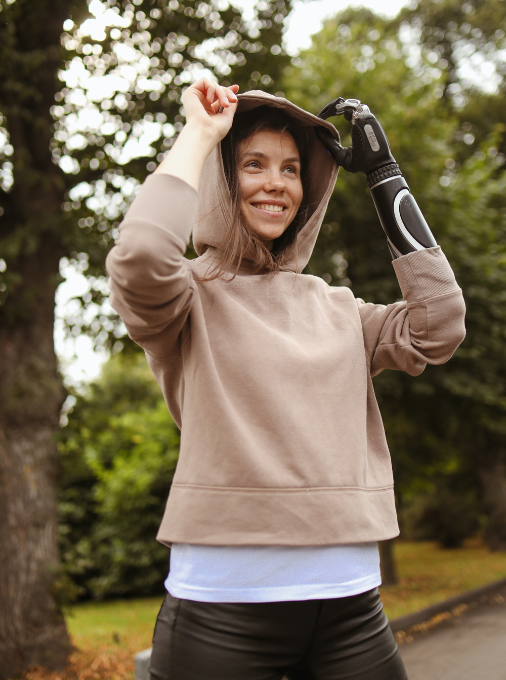 young woman with a prosthetic arm smiles in a park