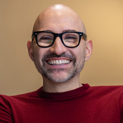 portrait of spencer west smiling wearing glasses and a red shirt